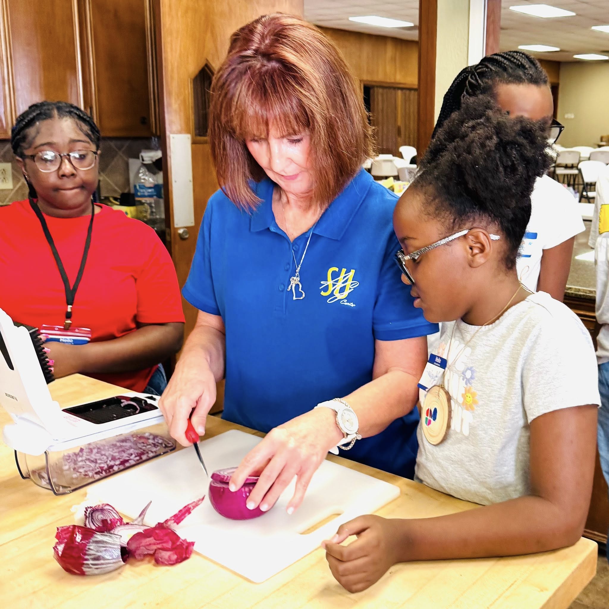 Two girls watching a woman slice a purple onion.